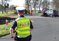 policjanci zabezpieczają miejsce zdarzenia, w tle na przejeździe kolejowym uszkodzony samochód