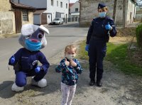 Policjantka wspólnie z sierż. Prudkiem - maskotką prudnickiej policji przekazuje maseczki dzieciom.