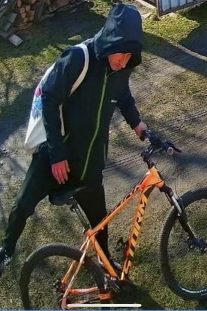 mężczyzna ubrany w czarna kurtkę z kapturem wsiadający na pomarańczowy rower
