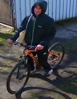 mężczyzna ubrany w czarna kurtkę z kapturem wsiadający na pomarańczowy rower