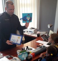 Policjant w mundurze odbiera od dzieci album z rysunkami i obrazek w ramce.