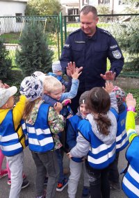 Dzieci przybijają piątkę dłońmi z policjantem w mundurze.