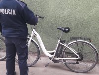 Mężczyzna w policyjnym mundurze stoi przy białym rowerze.