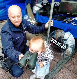 Zdjęcie przedstawia policjanta pokazującego sprzęt policyjny.