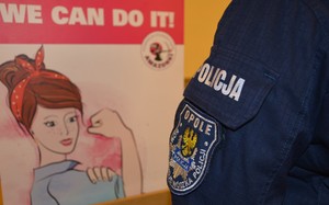 policjantka stojąca przy banerze z grafika kobiety i opisem w języku angielskim tłumaczonym na język polski o treści &quot;możemy wszystko&quot;