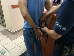 zatrzymany mężczyzna z kajdankami zapiętymi na ręce prowadzony przez policjantów