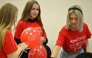 3 dziewczyny w czerwonych koszulkach trzymają balony z logo DKMS